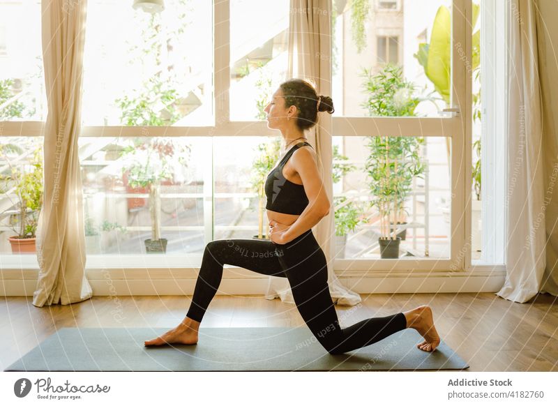 Woman preparing to perform Crescent Lunge on Knee pose indoors woman yoga crescent lunge on knee practice wellness healthy lifestyle vitality energy