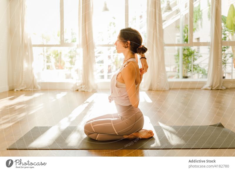 Concentrated woman stretching arms in Thunderbolt pose at home yoga hand behind back practice healthy lifestyle energy house eyes closed sunshine vitality