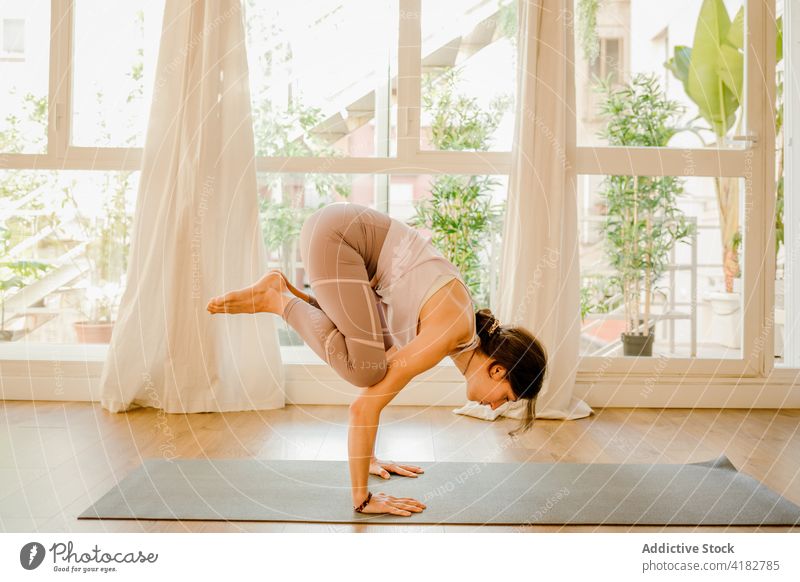 Woman showing Crow pose on yoga mat in house room woman balance crow pose handstand healthy lifestyle talent energy window kakasana inversion support practice