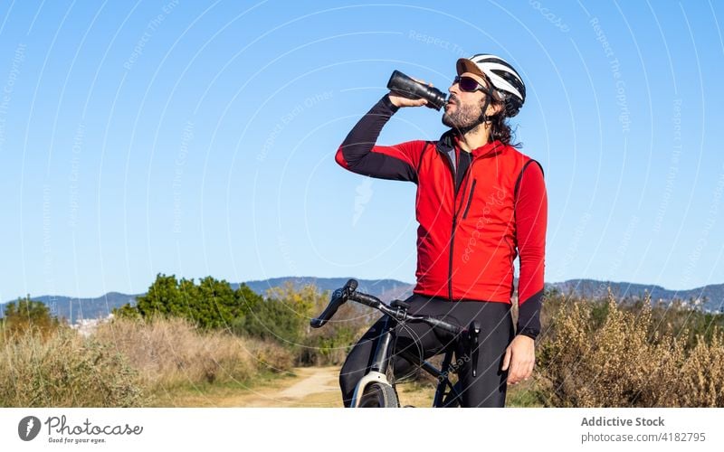 Cyclist drinking water after training in countryside cyclist bicycle rest break sporty man active male bicyclist workout lifestyle activity recreation athlete