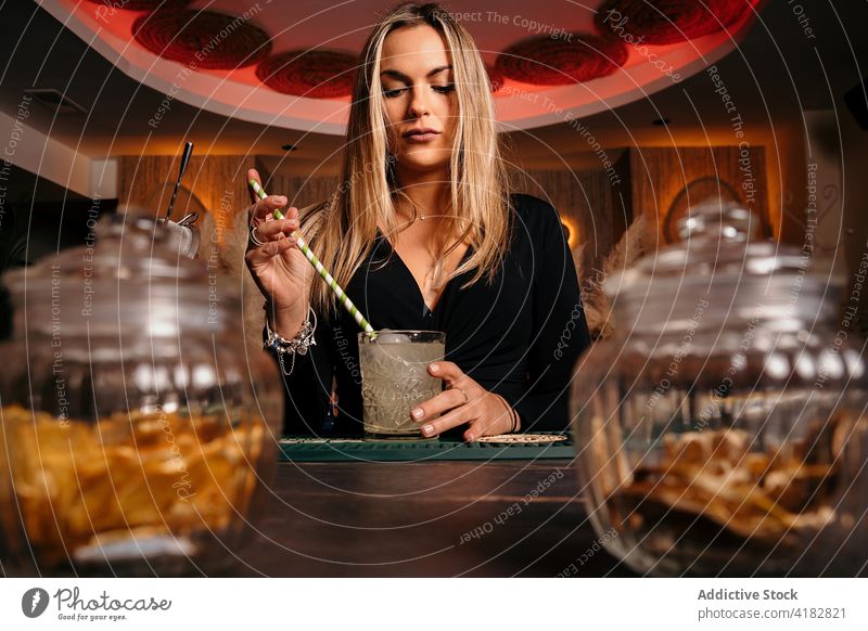 Woman mixing and serving cocktail during work in stylish bar woman stir serve alcohol straw bartender counter prepare drink beverage tasty female elegant blond