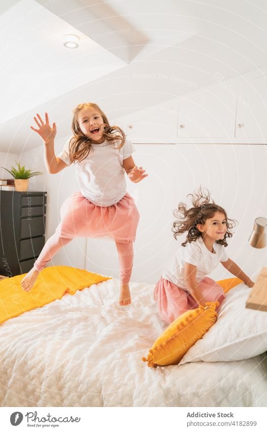 Happy sisters jumping on bed in excitement girl cheerful happy having fun glee joy sibling energy childhood kid casual excited carefree positive optimist