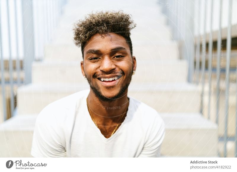 Smiling ethnic curly haired man looking at camera smile hipster beard young handsome cheerful happy stair male casual fence lifestyle black african american