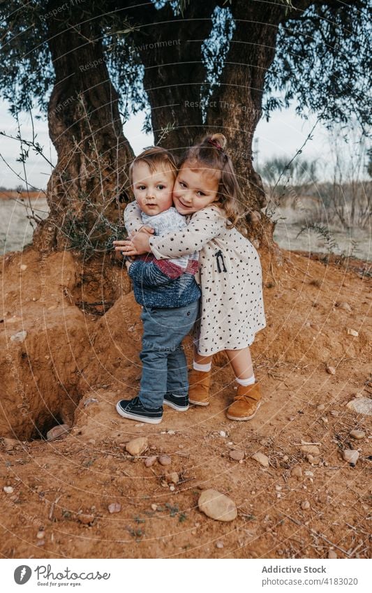 Cute siblings hugging near tree cuddle little brother sister cute love together meadow nature childhood happy relationship tender girl boy kid embrace affection
