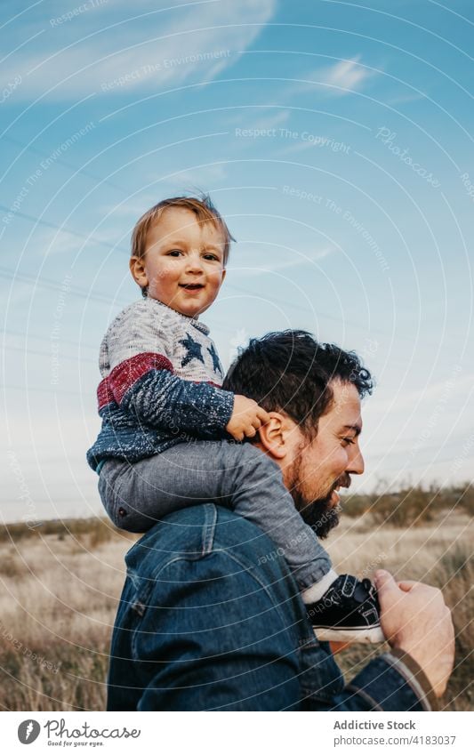 Man with cute child on shoulders in nature father ride cheerful care together boy son countryside weekend kid fatherhood joy childhood little glad parent
