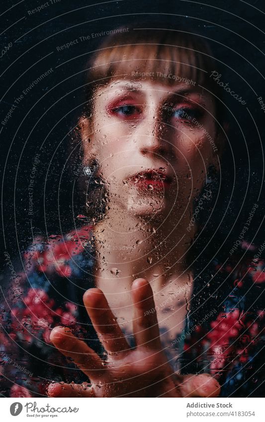 Melancholic woman with makeup touching glass with water drops melancholy depression sad solitude hopeless portrait gentle ornament bang red lips wear eyeshadow