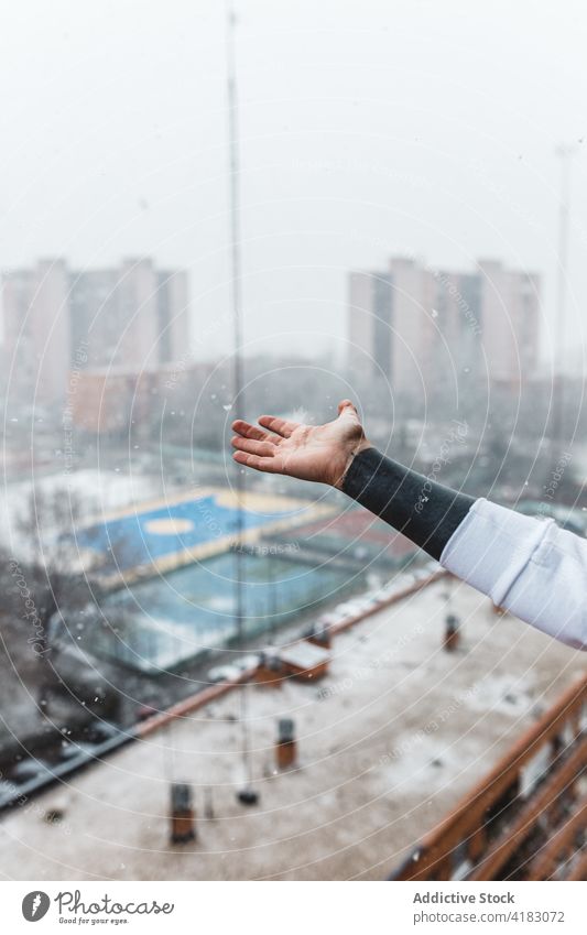 Crop faceless person catching snowflakes with hand on balcony snowfall winter city weather season urban cool joy frost cold street frozen glad blizzard freeze