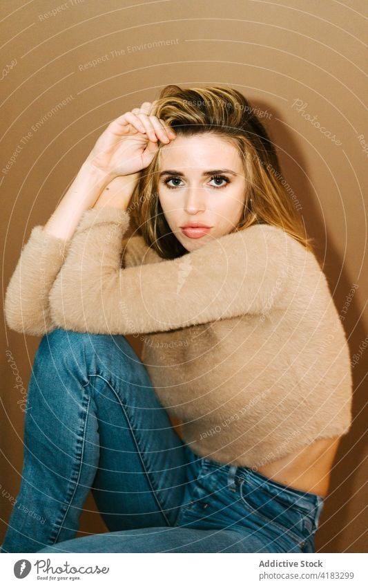 Stylish woman sitting in studio style trendy sweater young model touch hair confident fashion female jeans casual outfit appearance attire apparel garment cloth