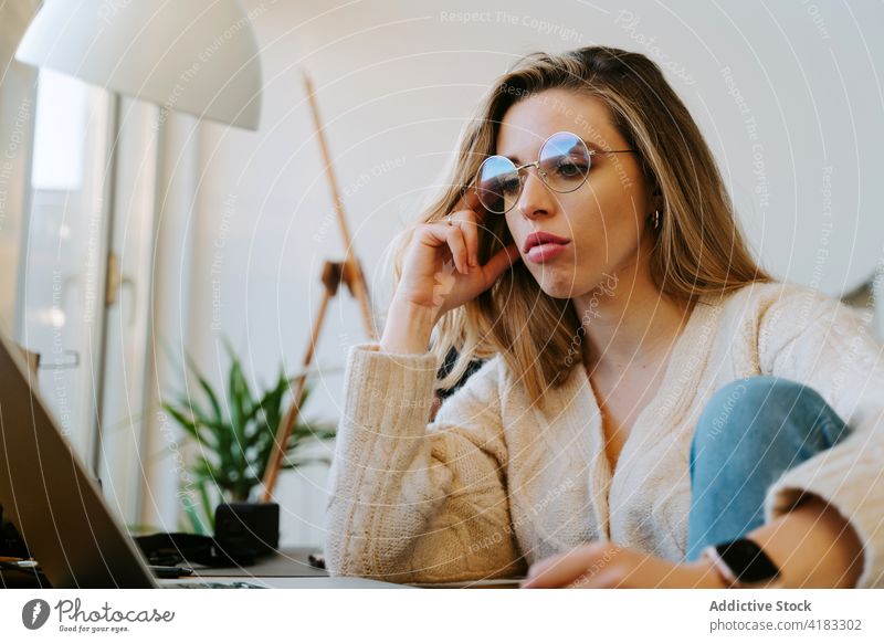 Young woman working on laptop at home freelance thoughtful remote project pensive startup read female browsing business occupation entrepreneur job think table
