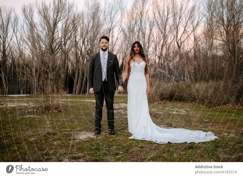 Elegant young multiracial newlywed couple holding hands in forest at sunset love wedding style together romantic nature leafless tree bride groom multiethnic