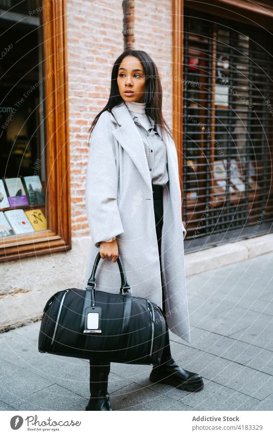 Stylish woman in coat standing on street trendy trench modern urban accessory bag pavement sidewalk lifestyle contemporary ethnic outfit confident town serious