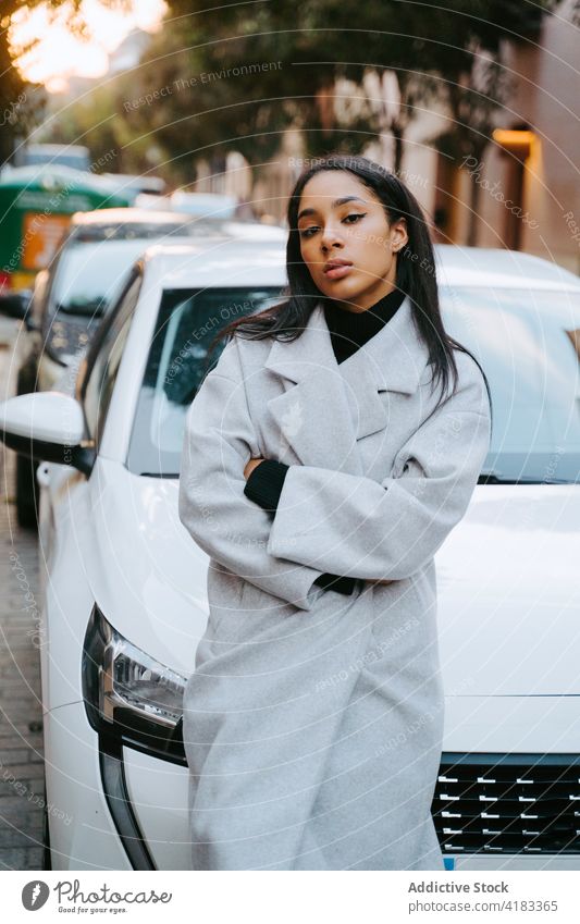 Confident ethnic woman at white car in city confident trendy street modern style owner driver lean on cool center young contemporary urban coat transport lady