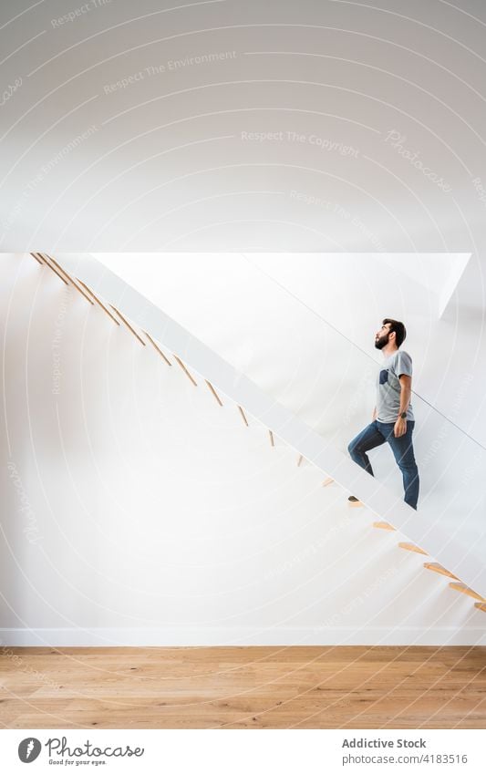 Man climbing up wooden stairs in house man climb up motion architecture symmetry geometry minimalism step floor contemporary style casual outfit jeans parquet