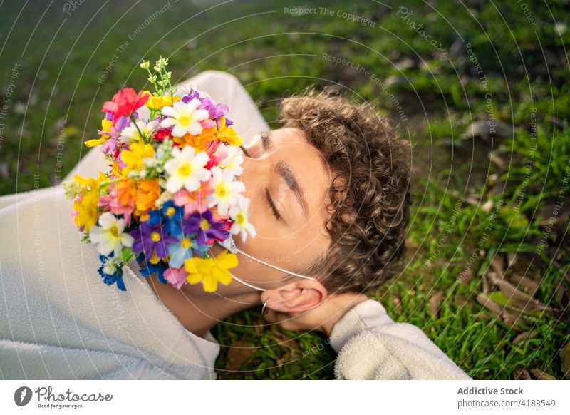 Unrecognizable man with flower mask on face resting on meadow covid concept eyes closed blossom bright lean on hand covid 19 protect bloom mindful summer