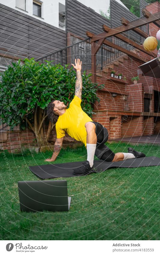Sportsman training on backyard and watching tutorial on laptop sportsman workout stretching plank exercise balance lesson courtyard male mat online wellness