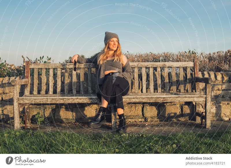 Happy woman in warm knitted wear resting on bench nature autumn cheerful happy traveler enjoy sunny young female lifestyle relax smile trendy positive chill