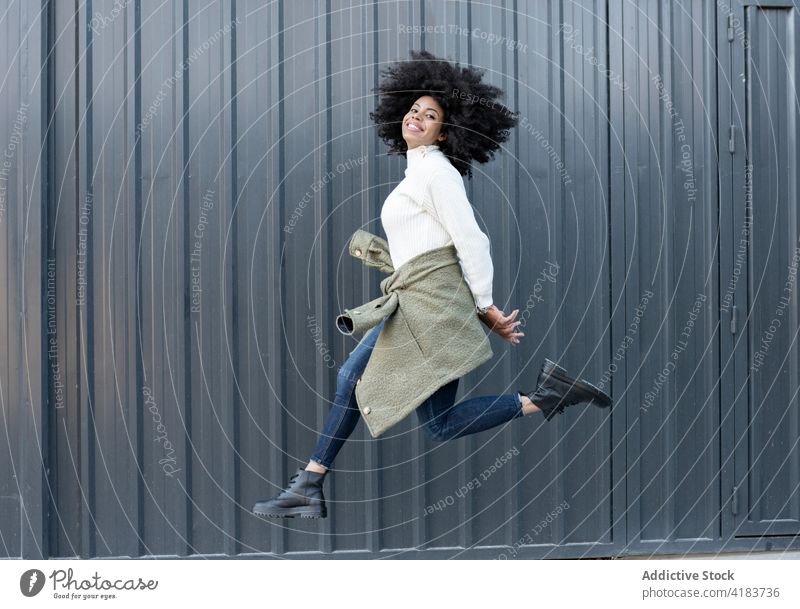 Confident young black female jumping on street woman smile trendy positive joy motion excited content energy expressive african american ethnic curly hair happy