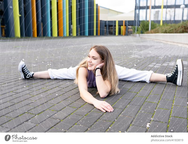 Content young woman doing split on pavement on street flexible stretch sporty energy gymnastic skill lean on hand acrobatic fit grace posture cheerful exercise