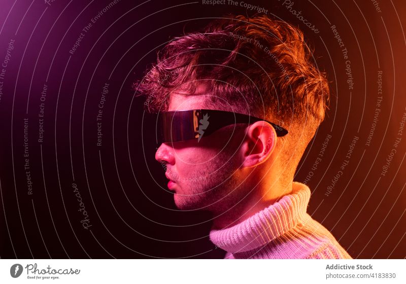Trendy young guy adjusting futuristic sunglasses in neon studio man style fashion self assured charismatic personality modern individuality male millennial