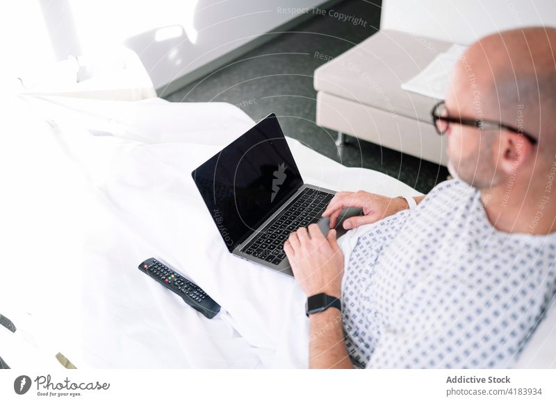 Serious male patient working on laptop on ward bed man serious focus workaholic hospital device clinic watch professional concentrate digital medicine sick ill