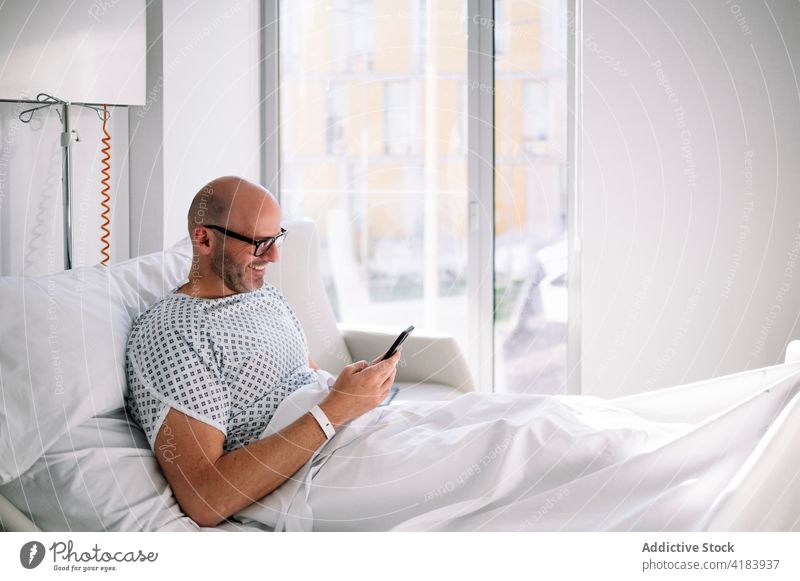 Happy male patient browsing phone on ward bed man smartphone using mobile focus workaholic device hospital clinic watch professional concentrate digital