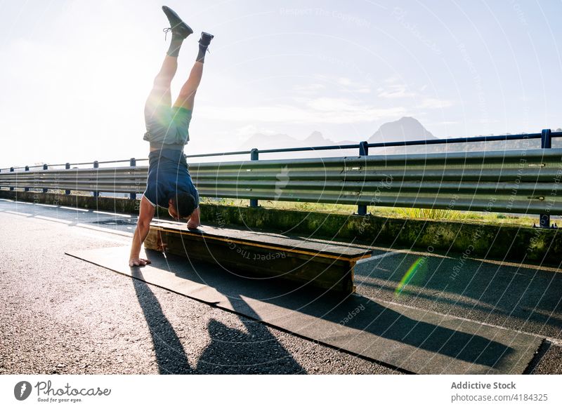 Anonymous disabled sportsman performing handstand on bridge in sunshine athlete balance workout training talent exercise countryside skill bench sky shadow