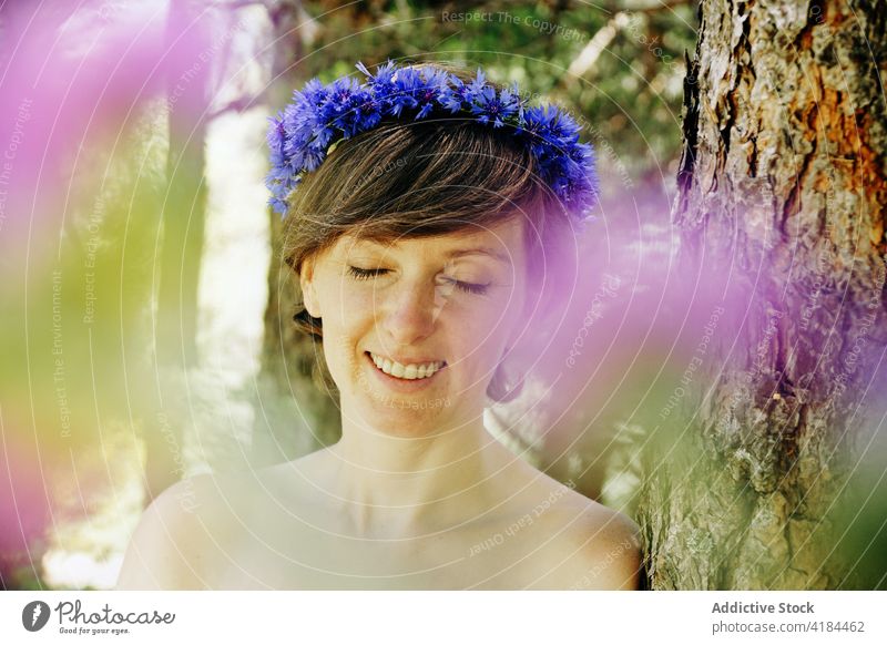 Romantic woman with wreath on head resting in park in sunlight forest peaceful calm romantic nature harmony style tree trunk female adult bare shoulders floral