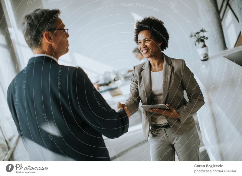 Businesswoman holding digital tablet and looking at handsome colleague while shaking hands in office happy smile executive worker businessman ethnic modern