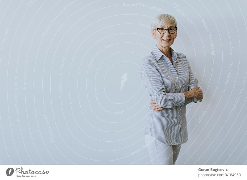 Mature businesswoman with arms crossed standing by the wall adult caucasian confident elderly eyeglasses female grey hair indoor indoors looking mature office