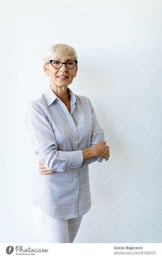 Mature businesswoman with arms crossed standing by the wall adult caucasian confident elderly eyeglasses female grey hair indoor indoors looking mature office