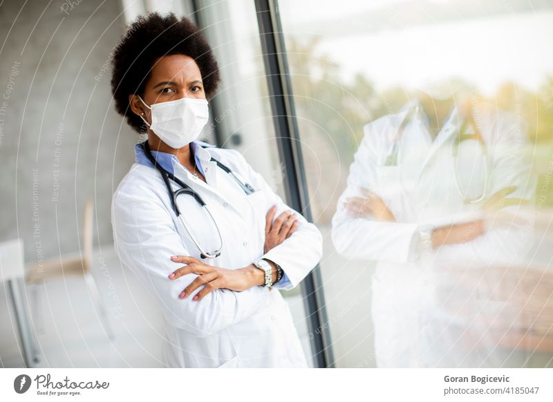 Black female doctor standing by the office window with facial protective mask adult black clinic contemplation displeased epidemic expertise females hospital