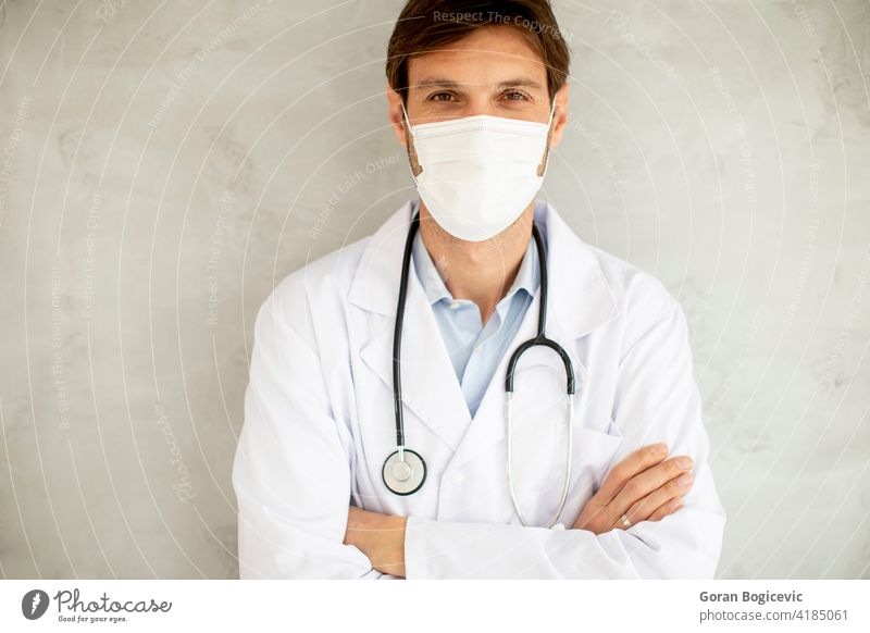 Attractive young male doctor wearing surgical mask and standing by the wall medical pandemic virus disease coronavirus health medicine clinic safety epidemic