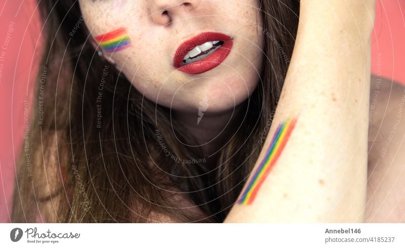 Portrait of a young woman with rainbow Flag on cheek and body, the LGBT community on a colorful pink background fashion hand pastel love person girl face beauty