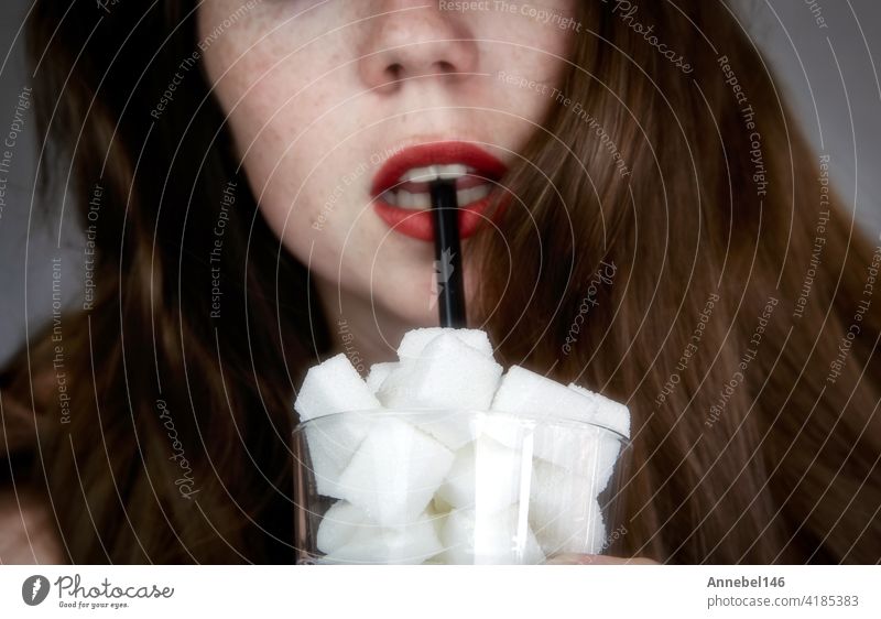 Portrait of young woman drinking with a black colored straw from a glass filled with sugar cubes Junk food, unhealthy diet, too much sugar on drinks, nutrition concept