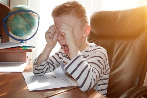 school-age boy crying and screaming while doing homework. the concept of heavy pressure education child student angry stress reading elementary young people kid