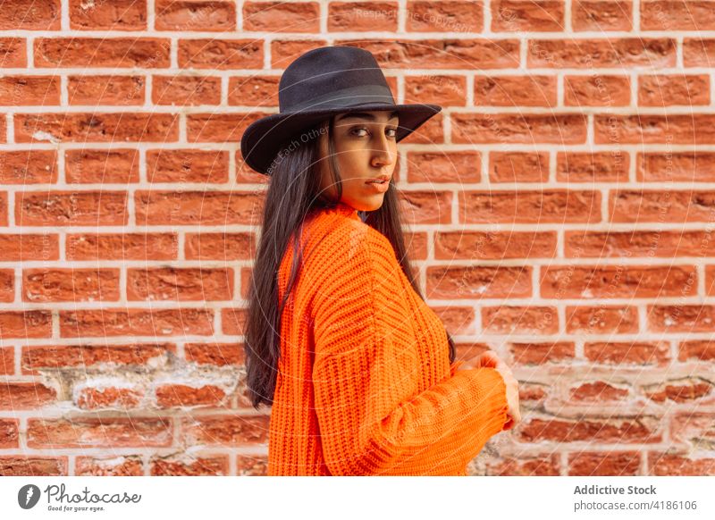 Stylish woman in hat standing near brick wall style fashion knitwear trendy color bright orange young ethnic female knitted lifestyle confident headgear modern