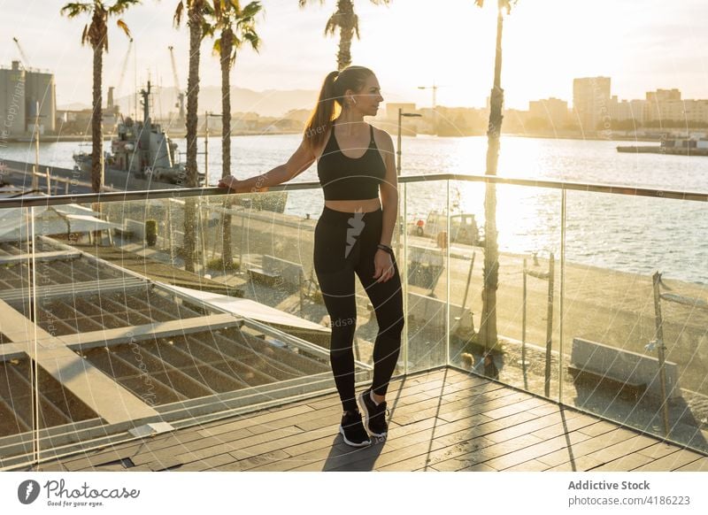 Fit woman in sportswear resting on embankment workout fit relax training sunset urban sporty slim female activewear lifestyle fitness wellness sportswoman