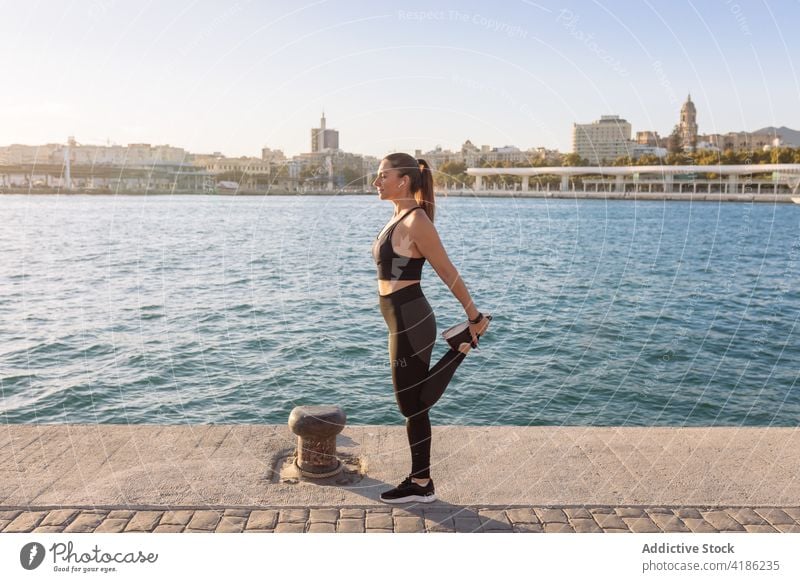 Slim sportswoman stretching legs on embankment workout exercise training fitness warm up female waterfront wellness healthy wellbeing athlete vitality lifestyle