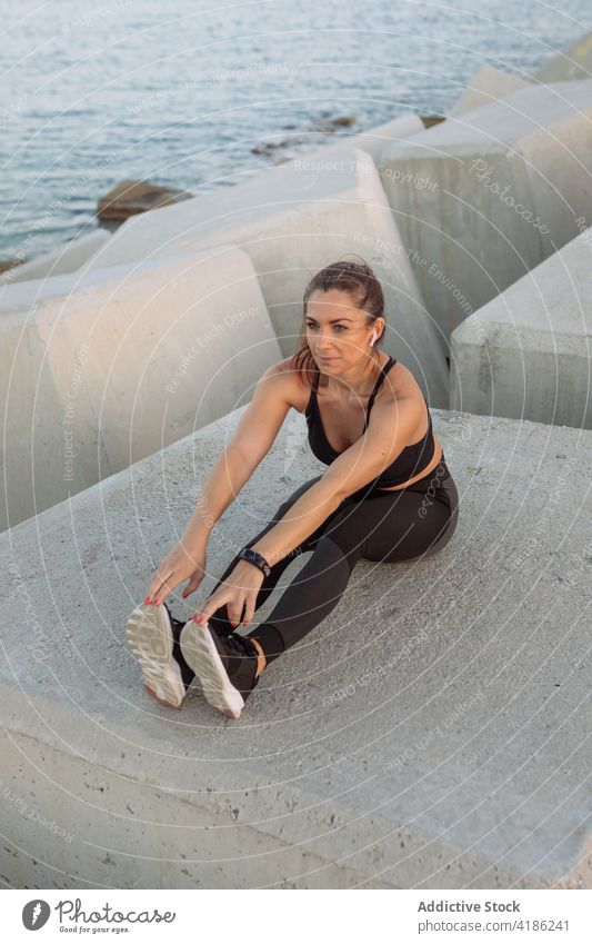 Sportswoman doing stretching exercise on breakwater sportswoman workout leg embankment training fitness active warm up female wellness healthy wellbeing runner
