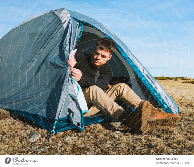 Serious young guy relaxing in tent in camp during hiking trip man rest trekking traveler trendy serious nature wanderlust hike male style tourism vacation
