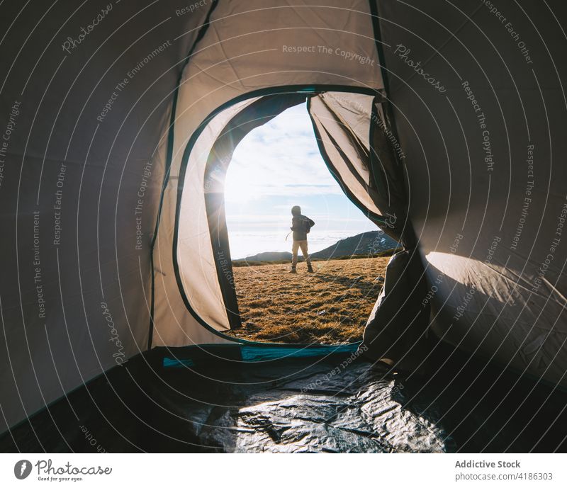 Anonymous hiker standing near tent at campsite on sunny day person traveler trip nature highland wanderlust morning journey warm clothes backpack explore