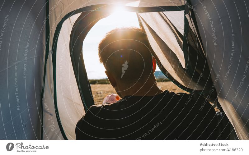 Anonymous male camper recreating in tent during hiking trip in highland man lying mountain nature hill hike traveler recreation relax landscape tourism casual