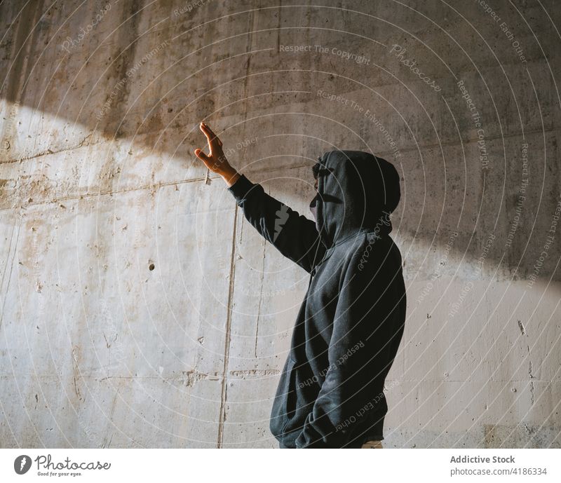 Anonymous guy standing on street and covering eyes from sunlight man cover face alone new normal style city cool shadow lonely concrete wall male young hoodie