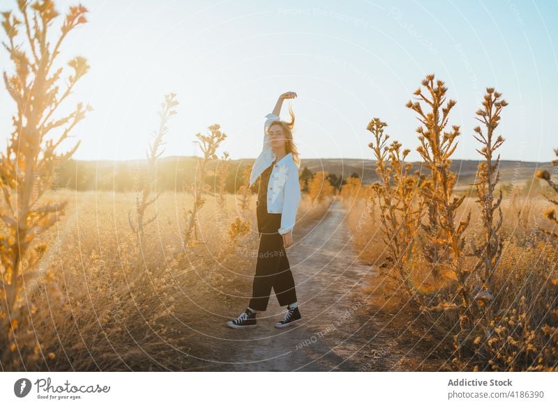 Stylish young woman dancing in countryside in sunlight dance field nature move confident style active holiday plant female trendy dry grass cloudless blue sky