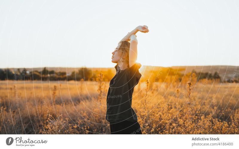 Relaxed young lady with raised arms in field woman arms raised enjoy countryside sunset relax nature landscape grace rest idyllic female casual summer grass