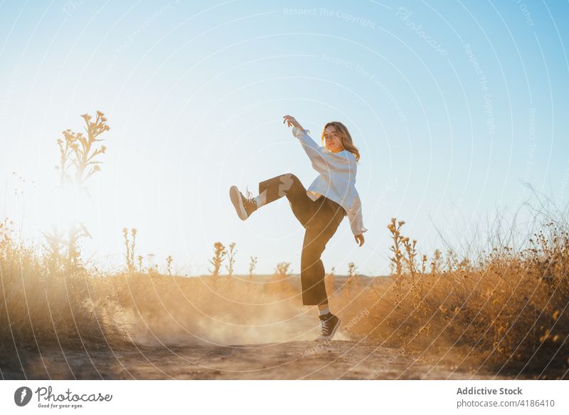 Stylish young woman dancing in countryside in sunlight dance field nature move confident style active holiday plant female trendy dry grass cloudless blue sky