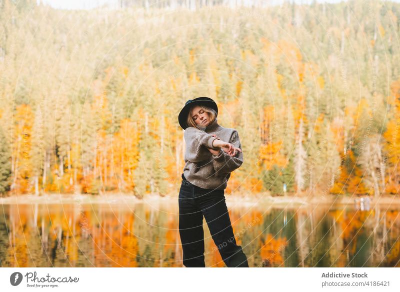 Stylish traveler in hat on shore against lake tourist cool style trip reflection tree woman sky stylish apparel garment confident trendy water mirror beautiful