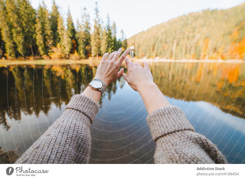 Crop traveler in wristwatch against lake reflecting autumn trees tourist highland reflection nature landscape contemplate woman accessory knitted wear admire