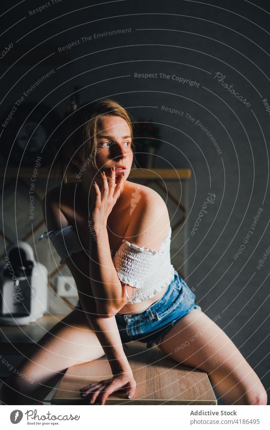 Pretty woman sitting on kitchen counter unemotional calm dreamy casual thoughtful feminine mug tranquil charming bare shoulders attractive beautiful lifestyle
