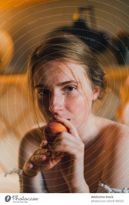 Beautiful woman with peach standing in modern kitchen dreamy snack serene positive lean on peaceful feminine counter tranquil charming bare shoulders attractive